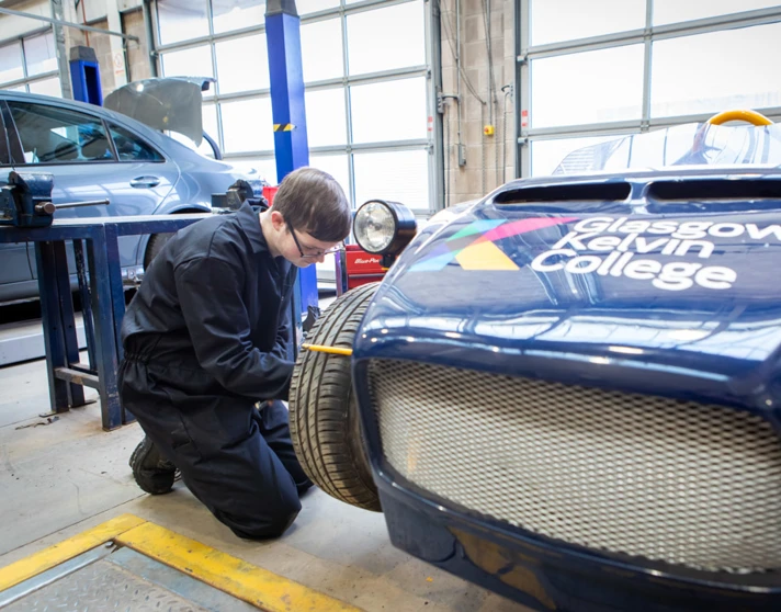 Student working on the front wheel of a Glasgow Kelvin College-branded kit car, checking its alignment and assembly. Student working on the front wheel of a Glasgow Kelvin College-branded kit car, checking its alignment and assembly.